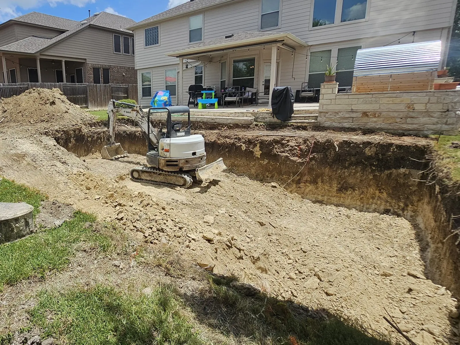 Small excavator digging a rectangular pool hole in a backyard