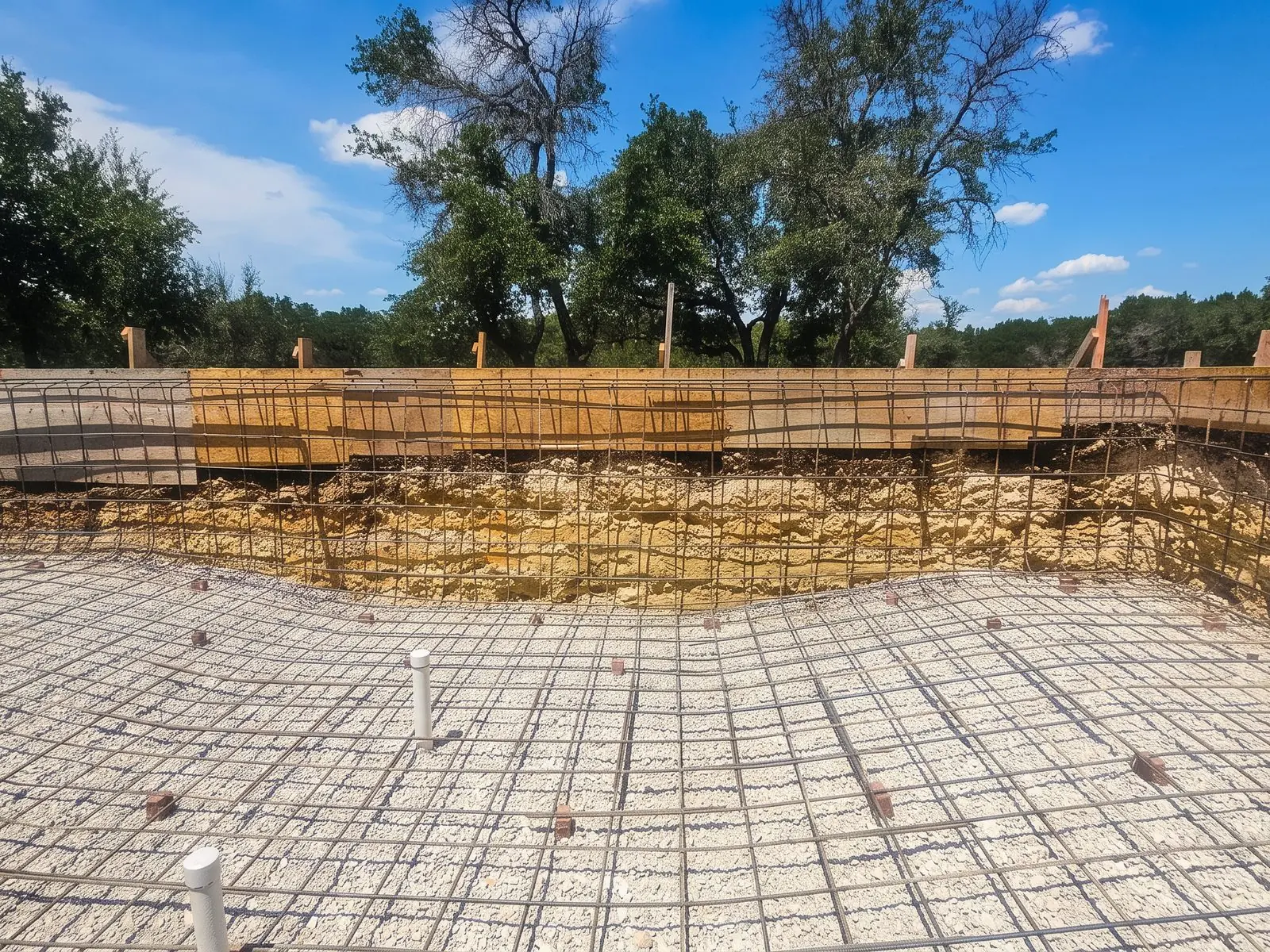Steel rebar grid tied over a gravel base across the floor and walls of a new pool