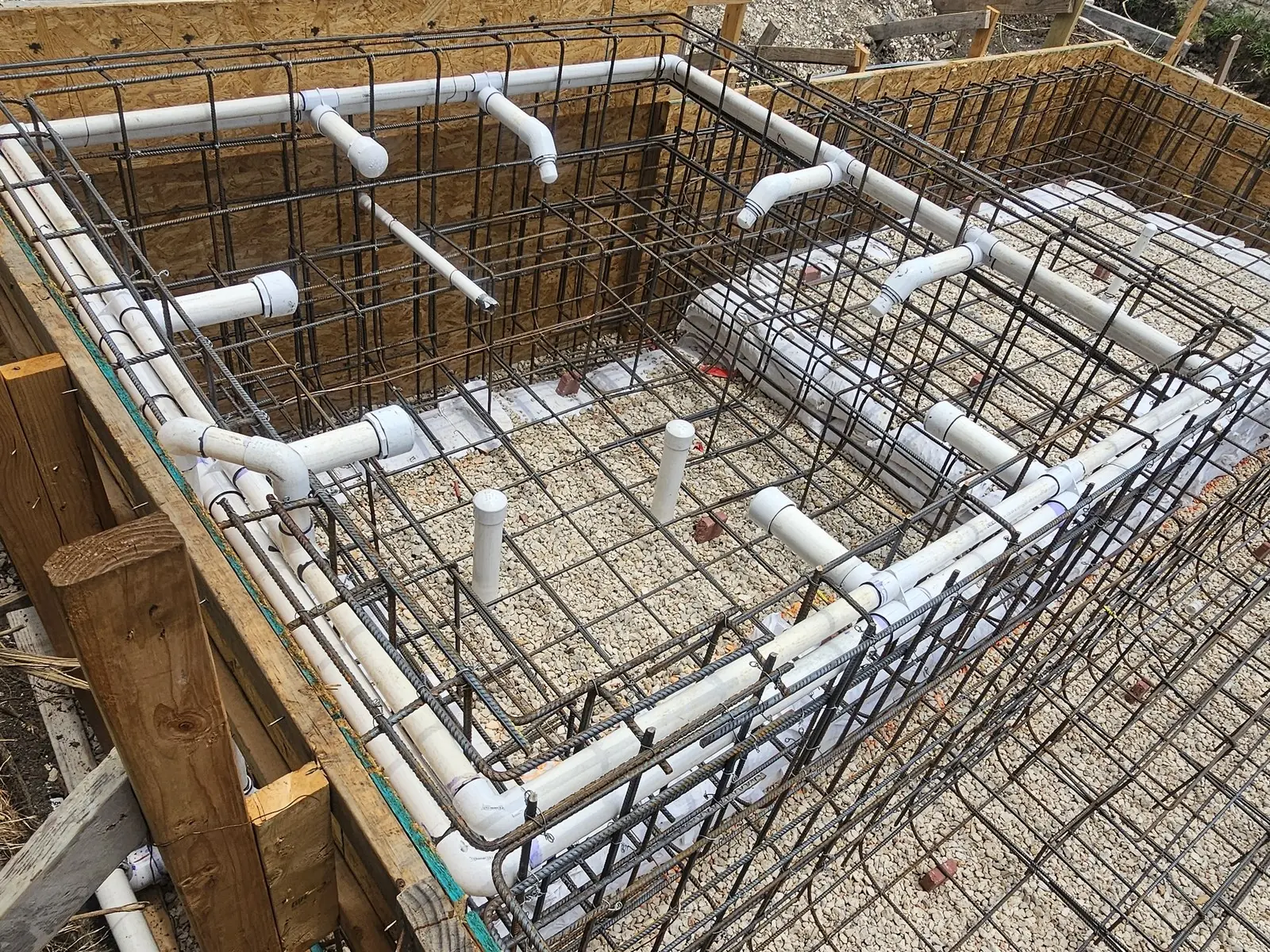 Spa plumbing on a new pool: a loop of white pipe with jet fittings run through the steel on a gravel base