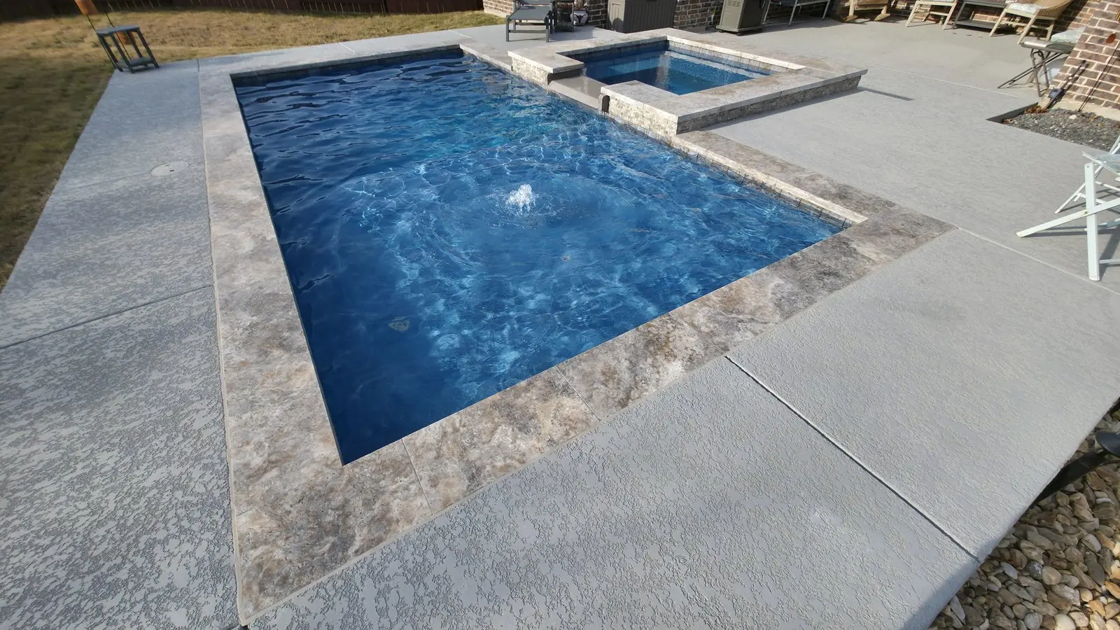 Rectangular pool with a raised spa, bubbler and travertine coping
