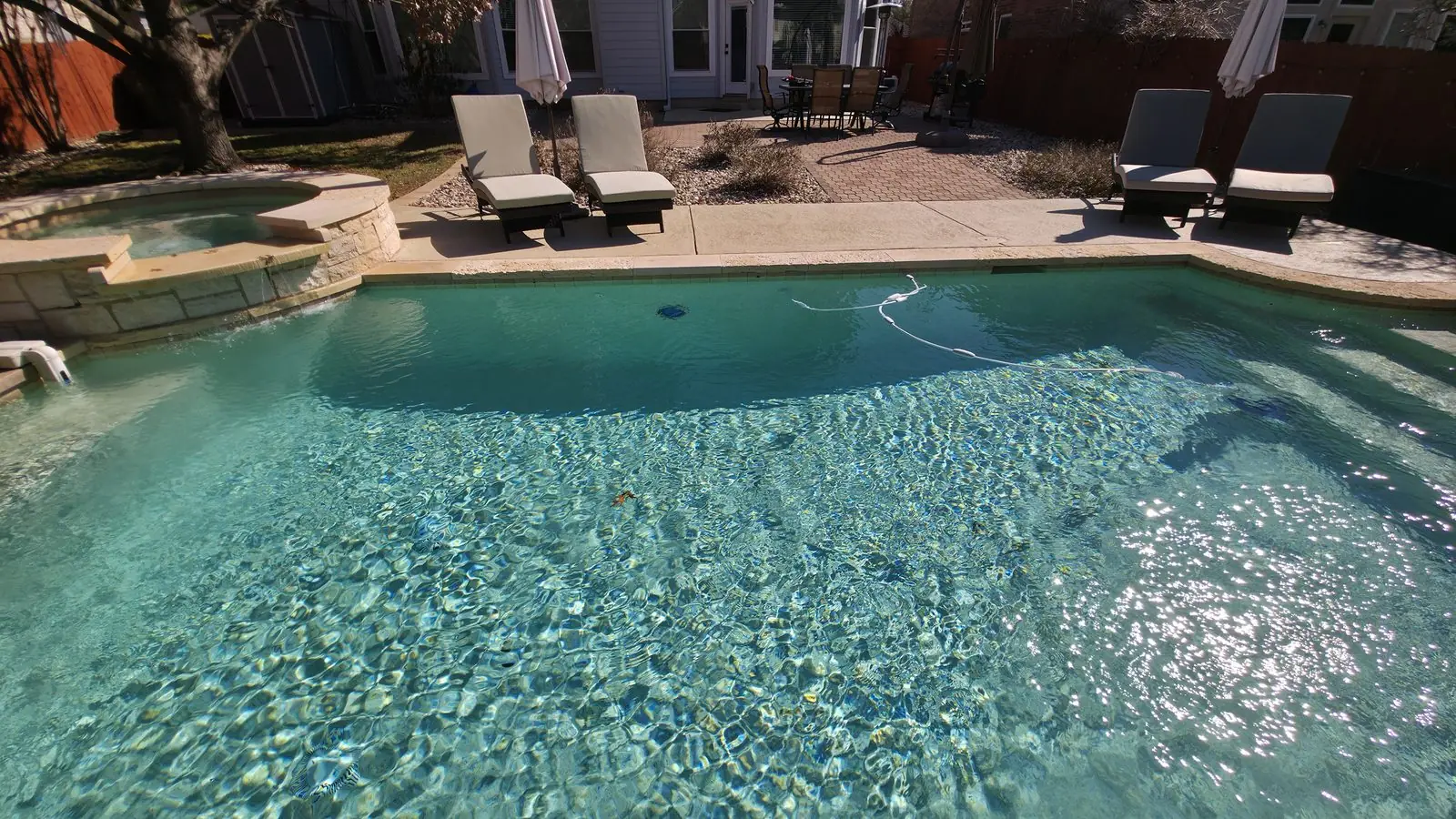 Turquoise pool with a round raised spa and patio seating