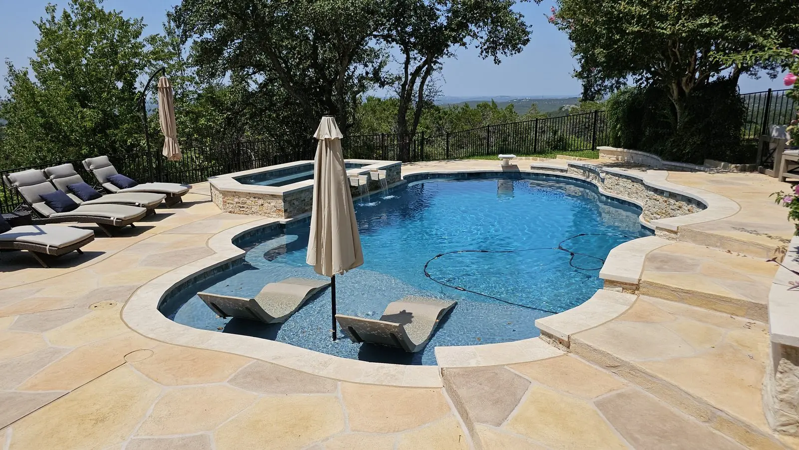 Freeform pool with raised spa, umbrella and ledge loungers