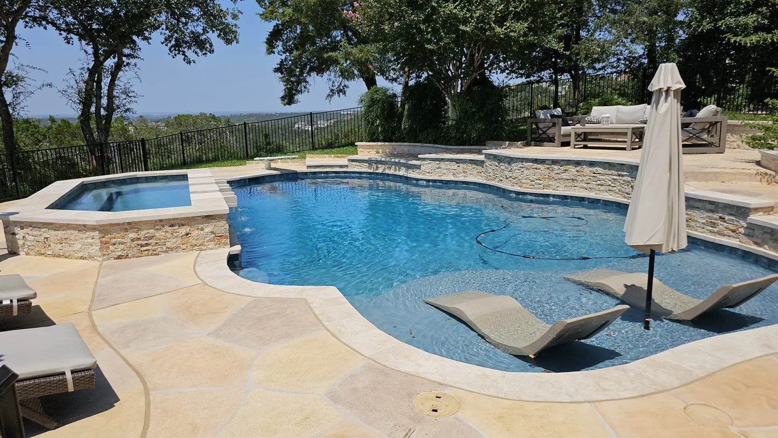 Freeform pool with tanning ledge loungers, raised spa and flagstone deck above a hill view