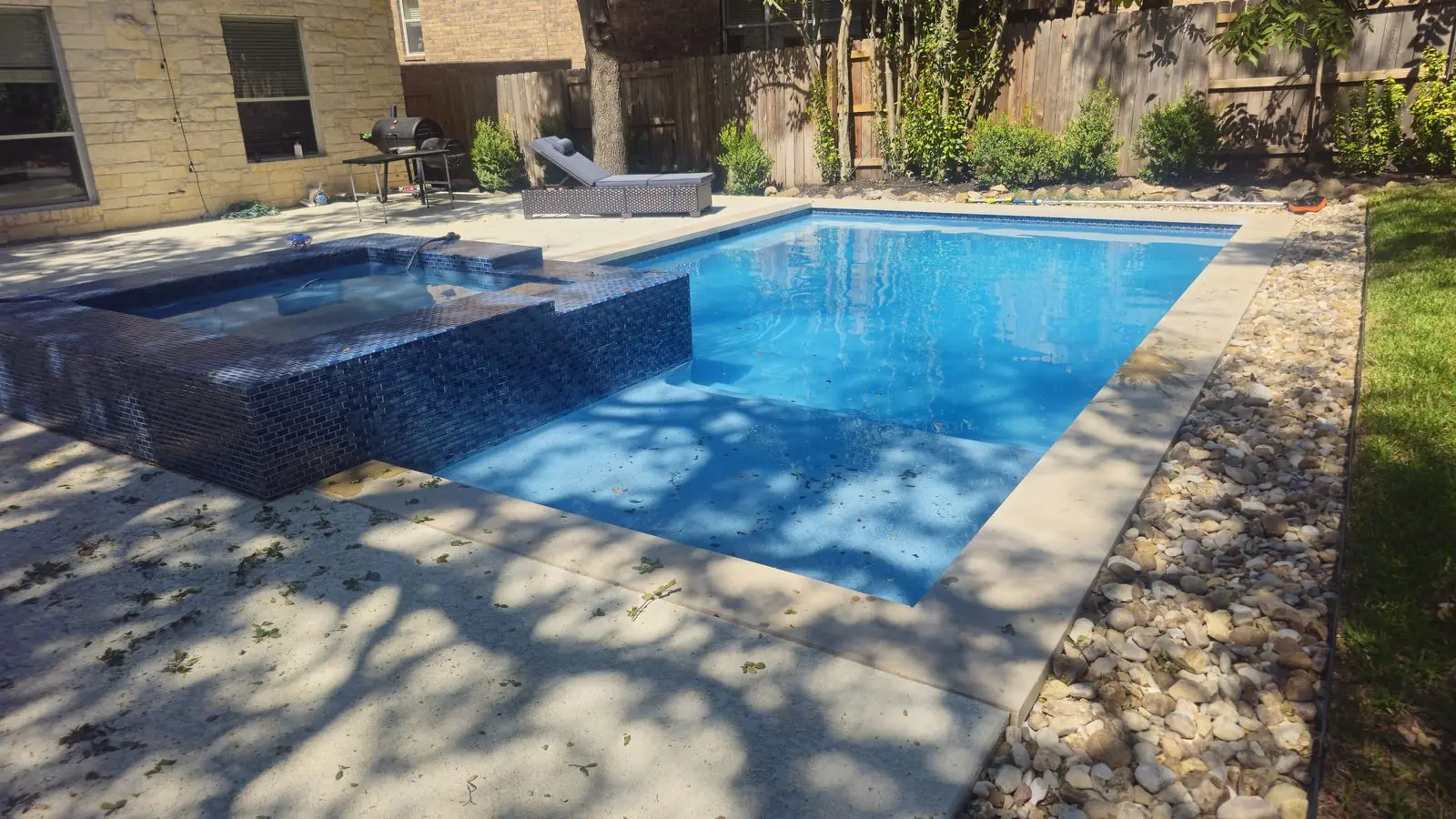 Rectangular pool with a raised glass-tile spa and river-rock border