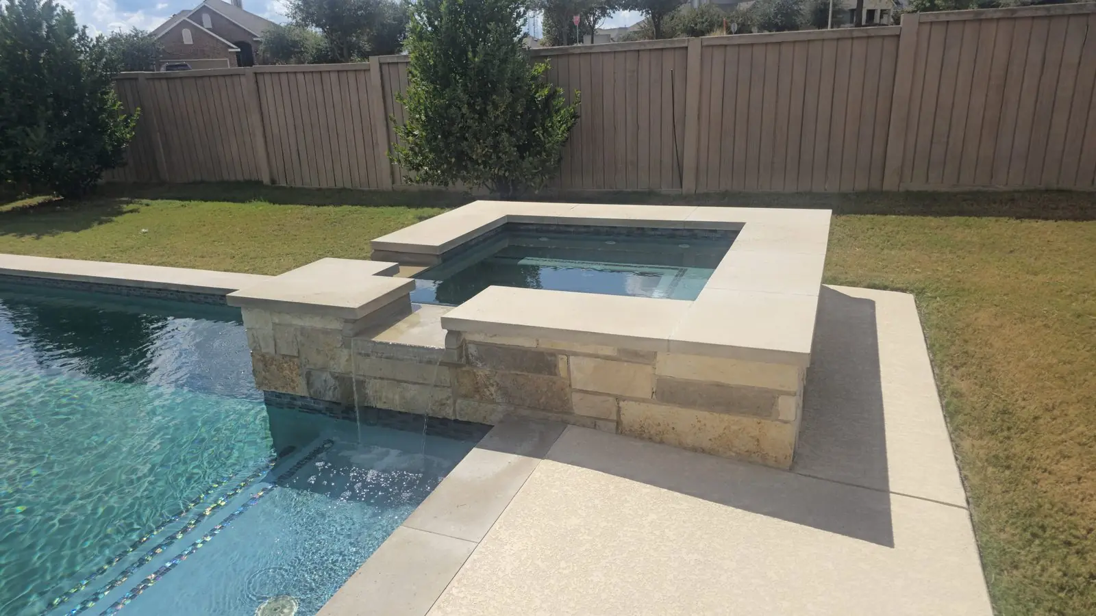 Square raised stone spa with a spillway into a pool with glass waterline tile