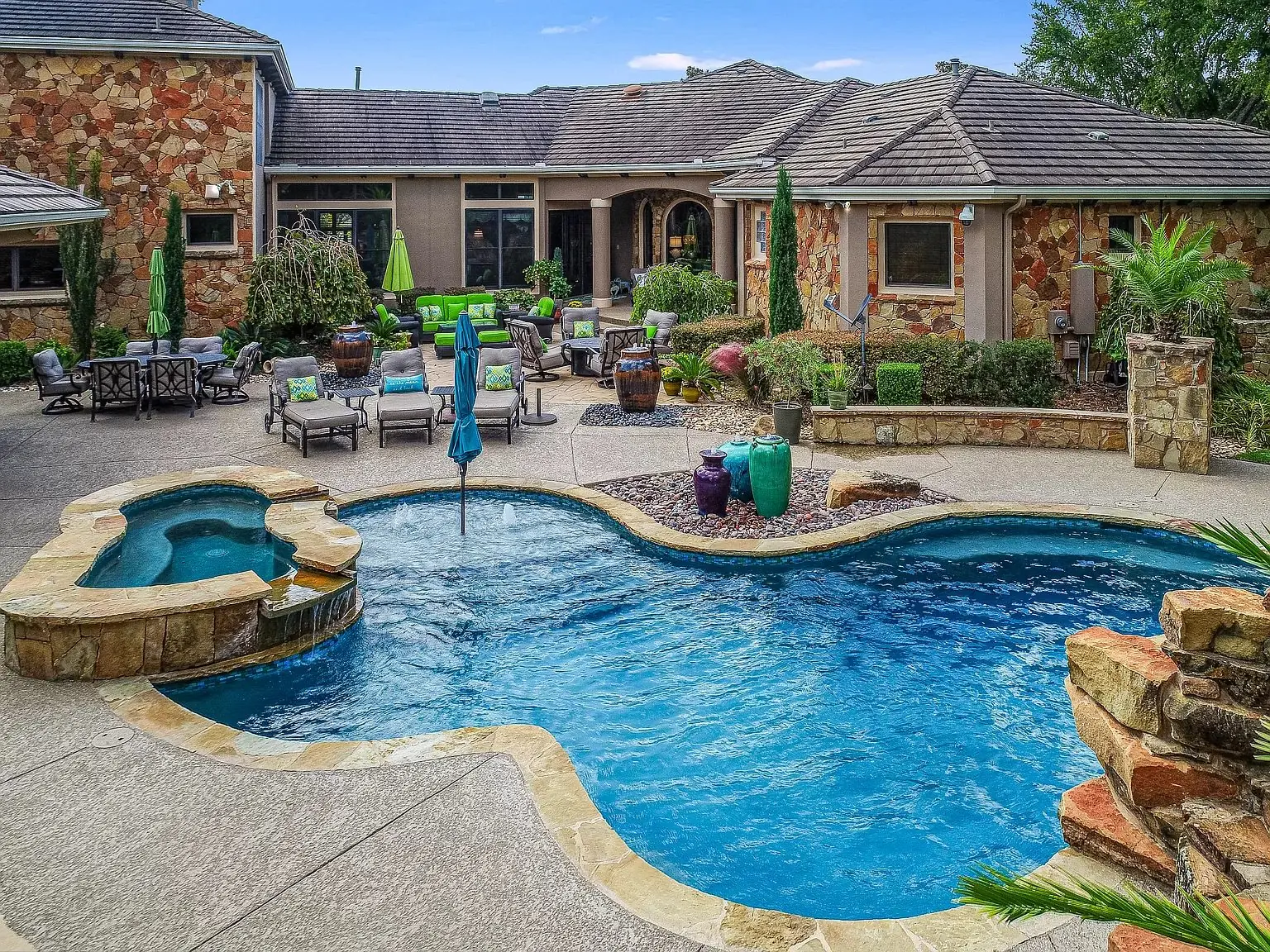 Freeform pool with fountain and stone waterfall behind a stone home, built by A&B Pools