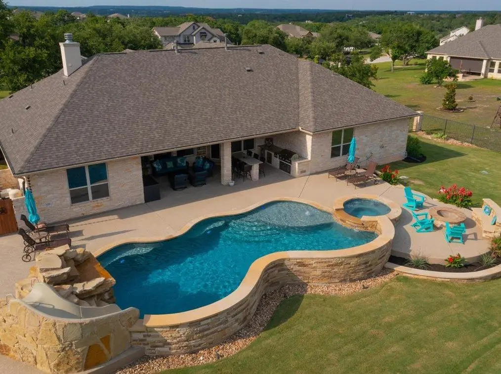 Aerial view of a freeform pool and spa behind a home