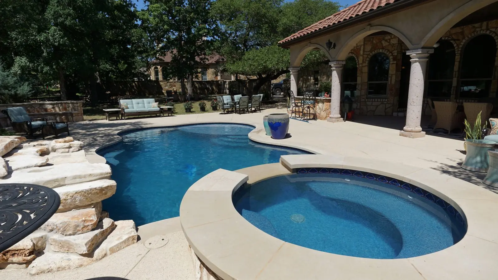 Freeform pool with round spa beside a covered patio