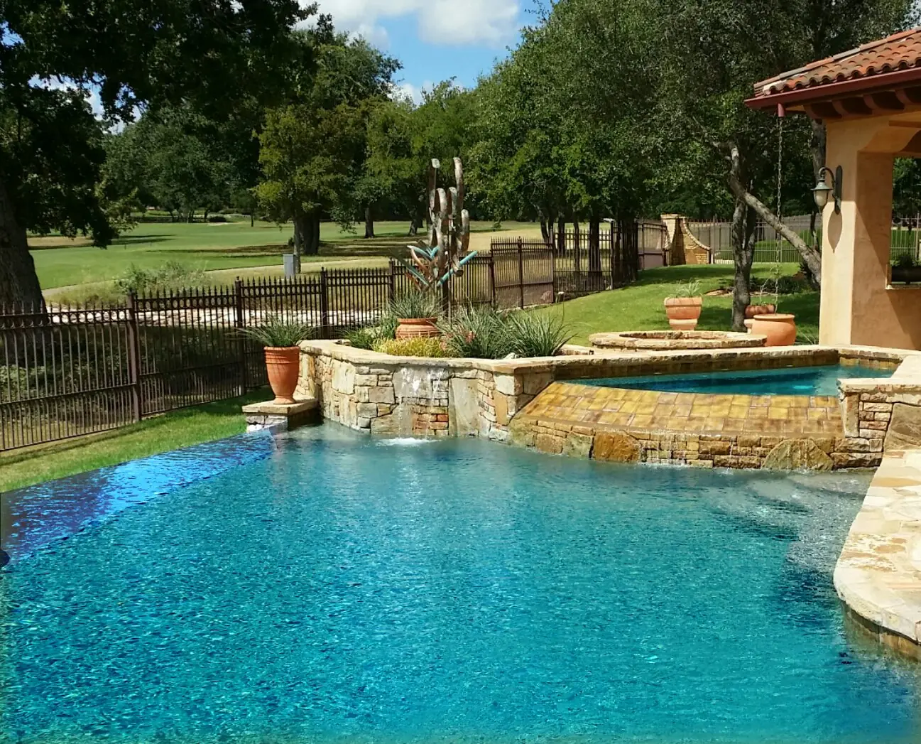 Pool with raised stone wall beside open lawn and oaks