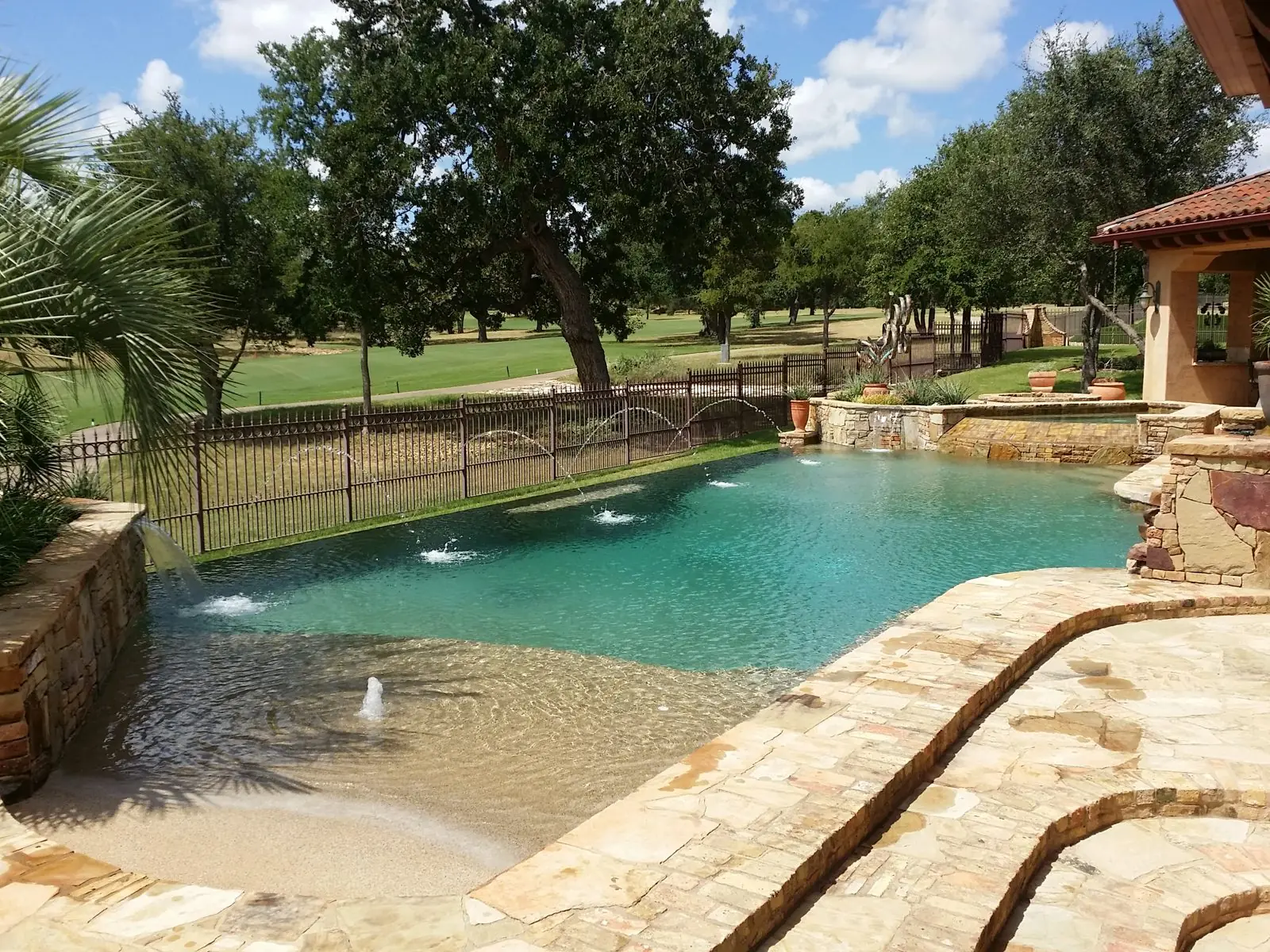 Pool with beach entry and raised stone spa overlooking open lawn