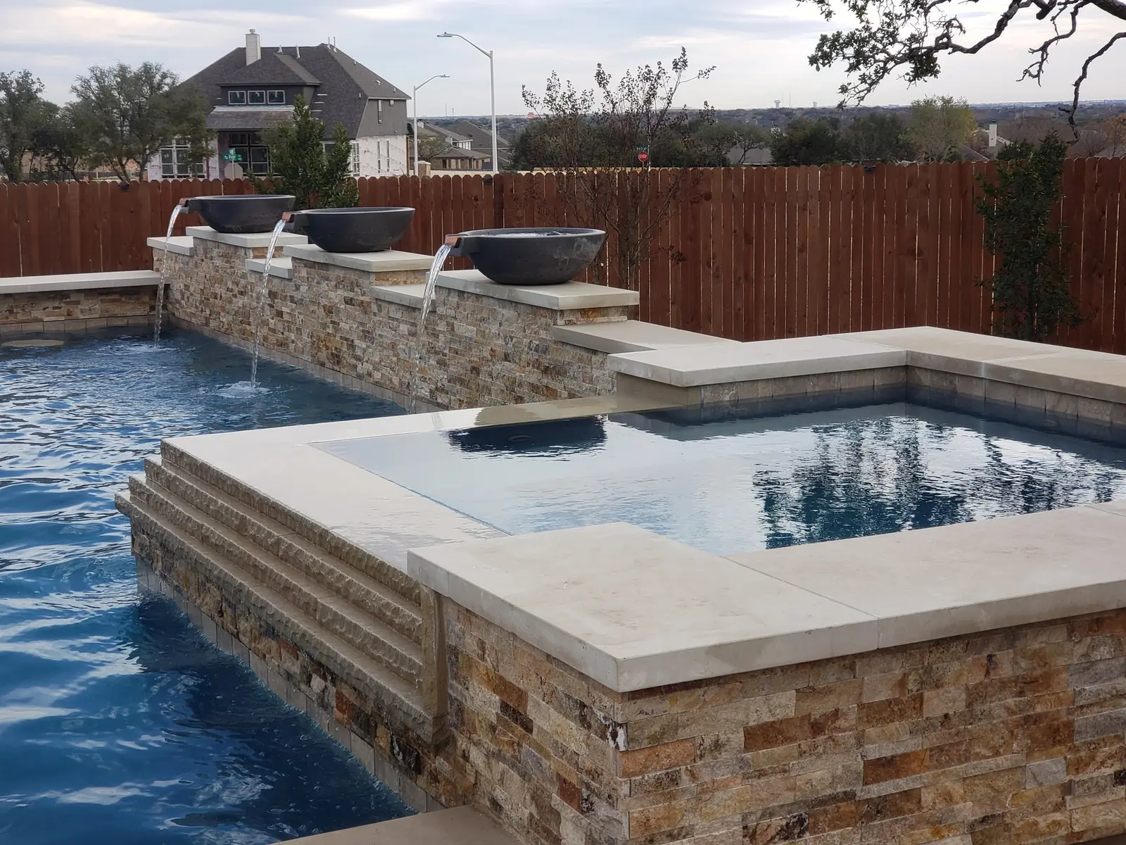Three water bowls pouring into a pool beside a raised stone spa
