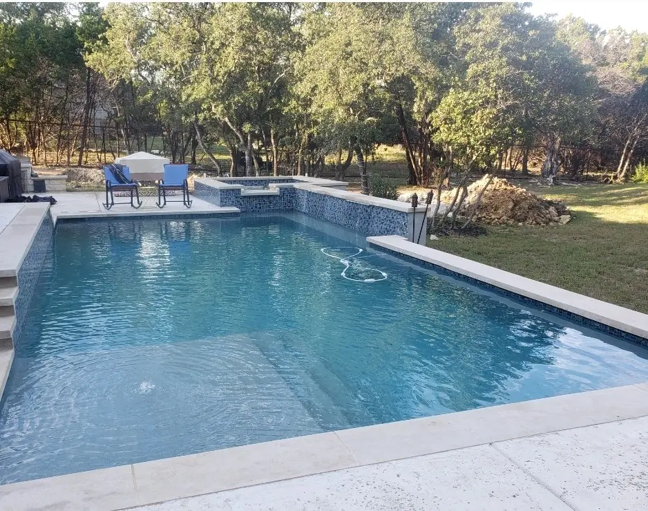 Rectangular pool with a raised blue-tiled spa and limestone coping under oak trees