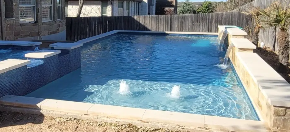 Rectangular pool with bubblers on a tanning ledge and sheer waterfalls from a stone wall
