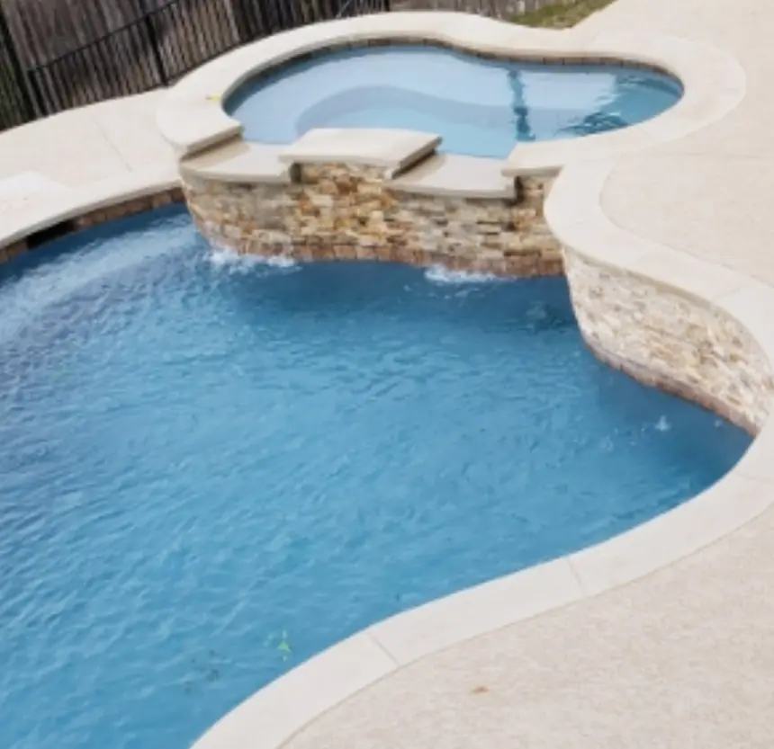 Freeform pool with a raised stacked-stone spa spilling into blue water