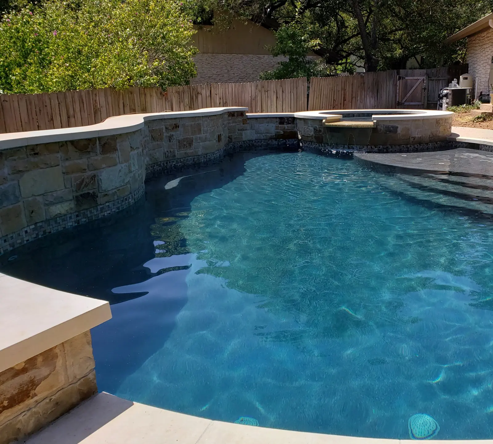 Freeform pool with a curved stone wall, mosaic tile band and raised spa
