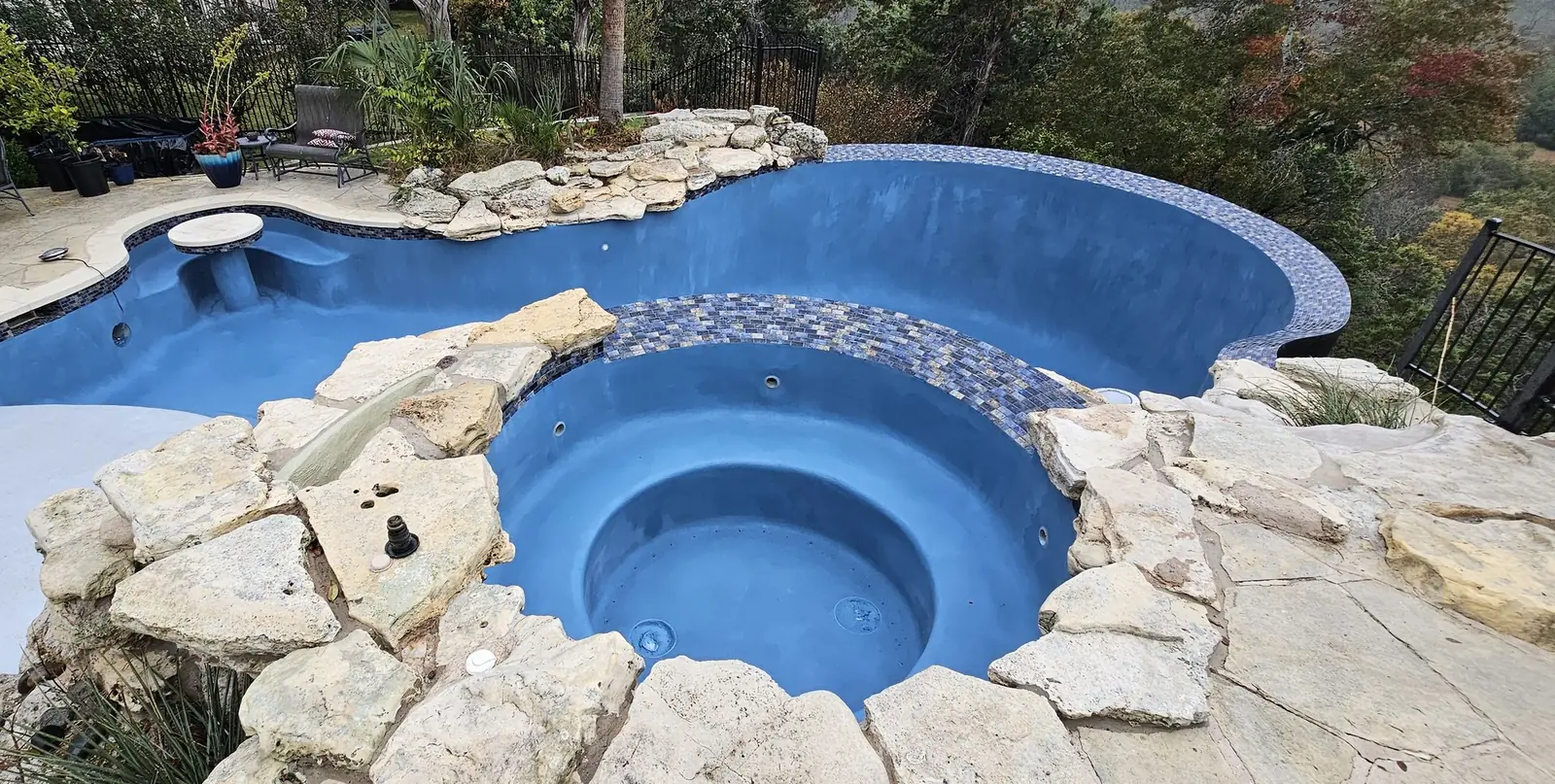 Empty pool and round spa with new blue plaster, mosaic tile and natural boulders