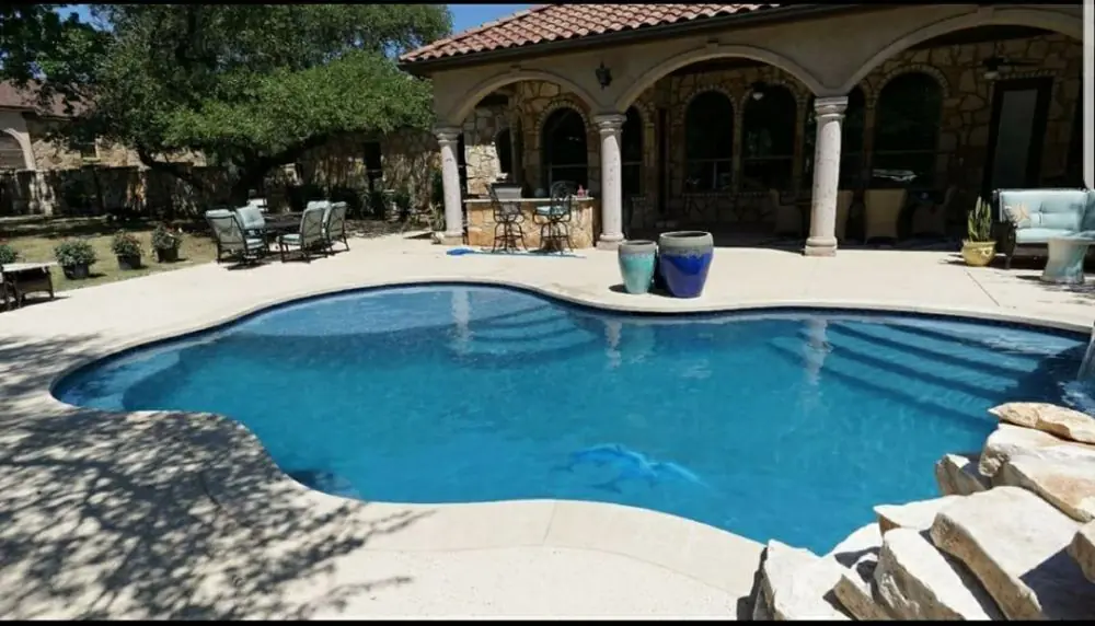 Freeform pool in front of an arched, columned patio