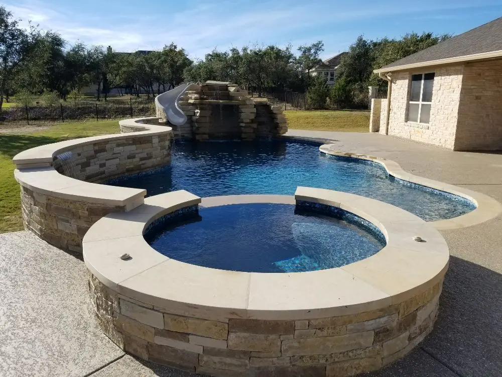 Round stone spa in front of a pool with rock waterfall