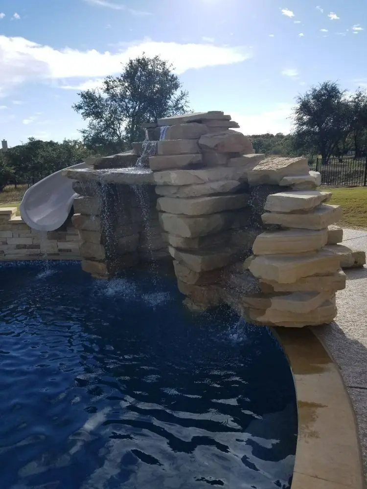 Stacked-rock waterfall with slide over blue water