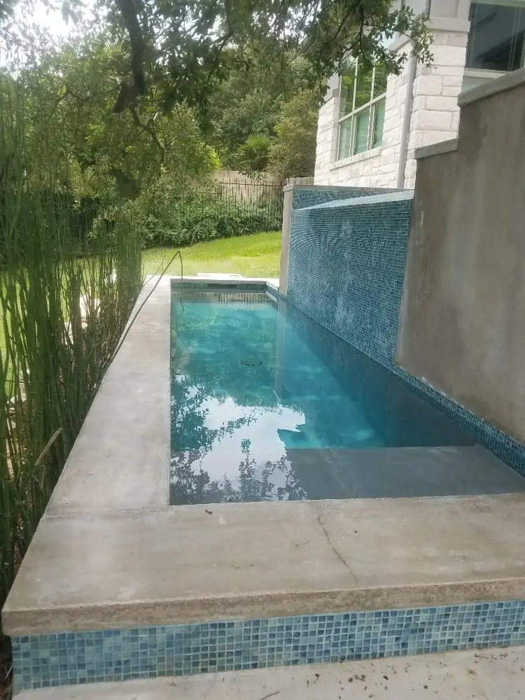 Narrow plunge pool beside a house with a glass-tile wall